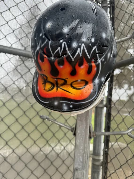 A flamed-up batting helmet hanging on the dugout fence.